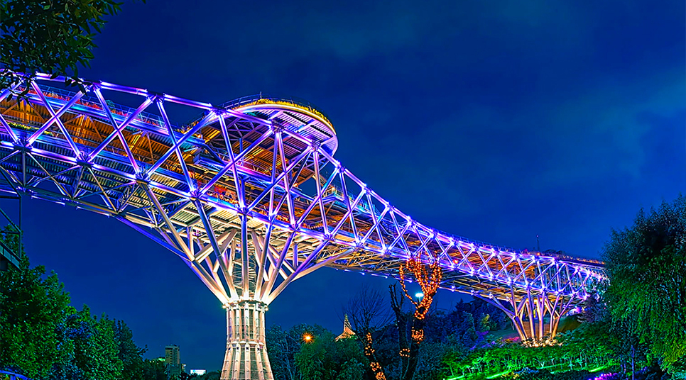 عکس از پل طبیعت در آسمان شب با نورهای بنفش و آبی و زرد روی آن